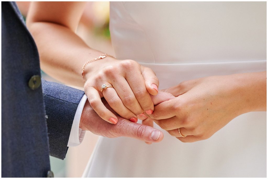 Bride and groom holding hands featuring a close up of their rings