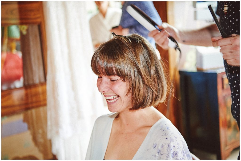 cool bride laughing whilst having her hair styled on wedding day