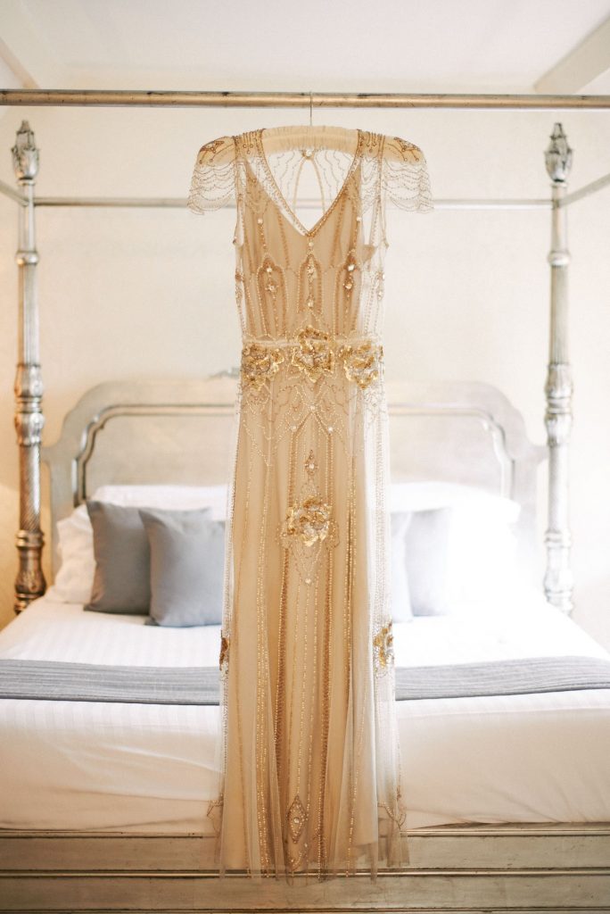Jenny Peckham vintage wedding dress with gold sequins hung on white 4 poster bed in bridal suite at Woodhall Manor