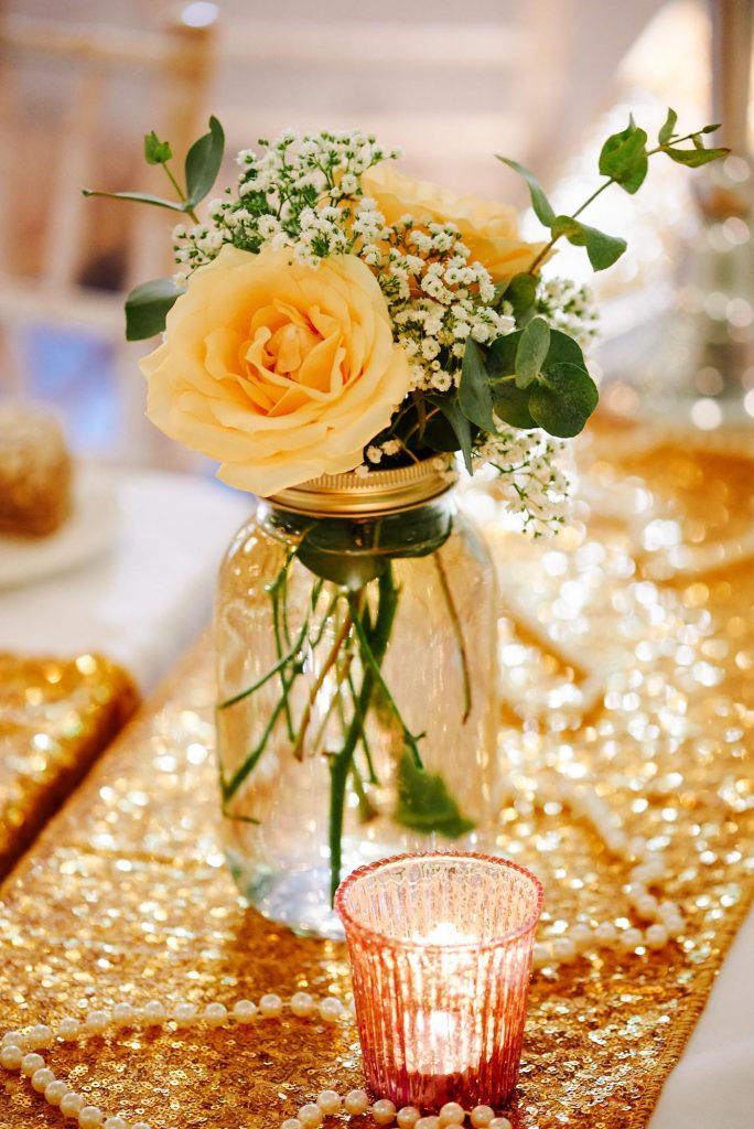 yellow rose in a jar on wedding table with gold sequined table runners.
