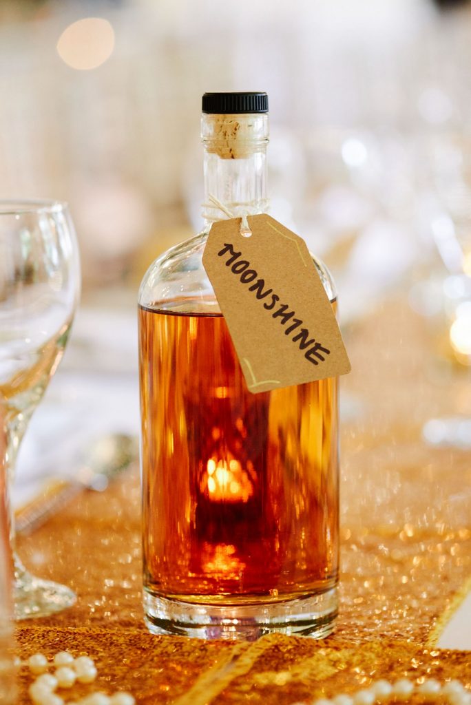 Bottle of moonshine on gold sequined wedding table at Great Gatsby themed wedding