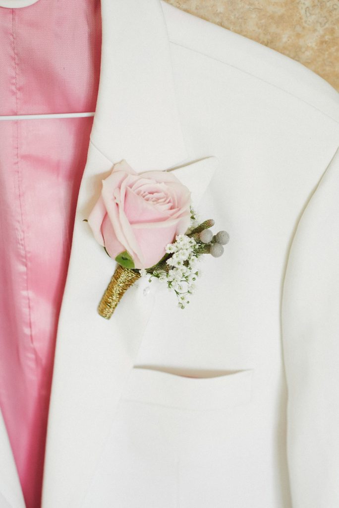 White groom suit with pink rose corsage pinned to the pocket