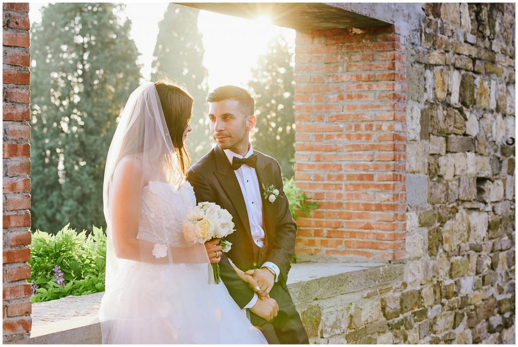 bride and groom sat on castle wall during sunset at Castello Di Vincigliata