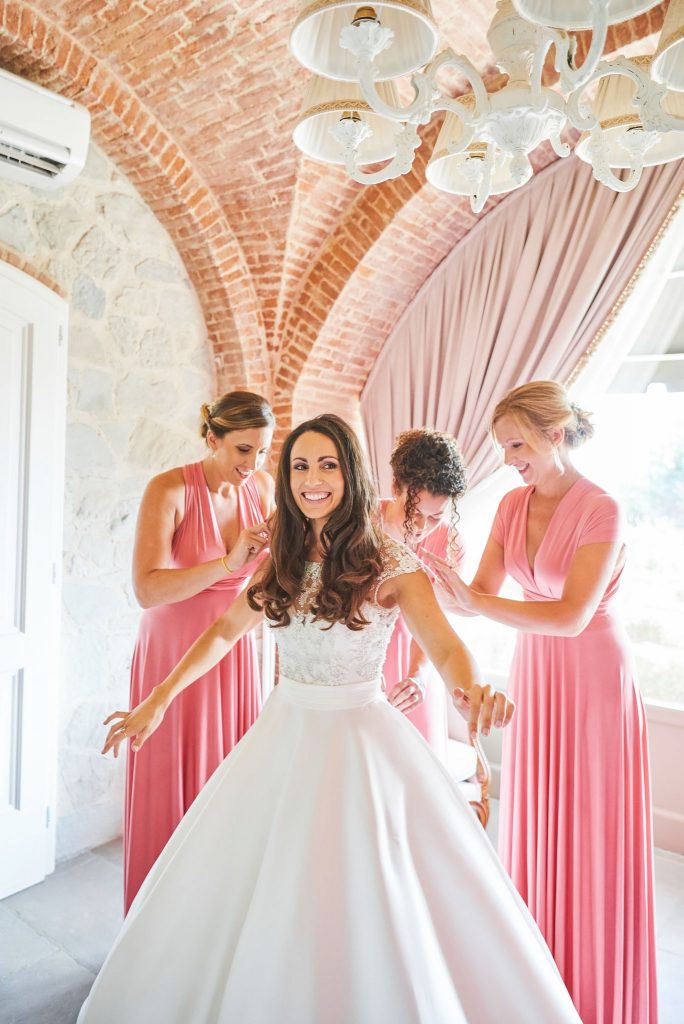 Bride laughing whilst her bridesmaids help put on her wedding dress at Villa le Fontanelle wedding venue in Florence, Italy