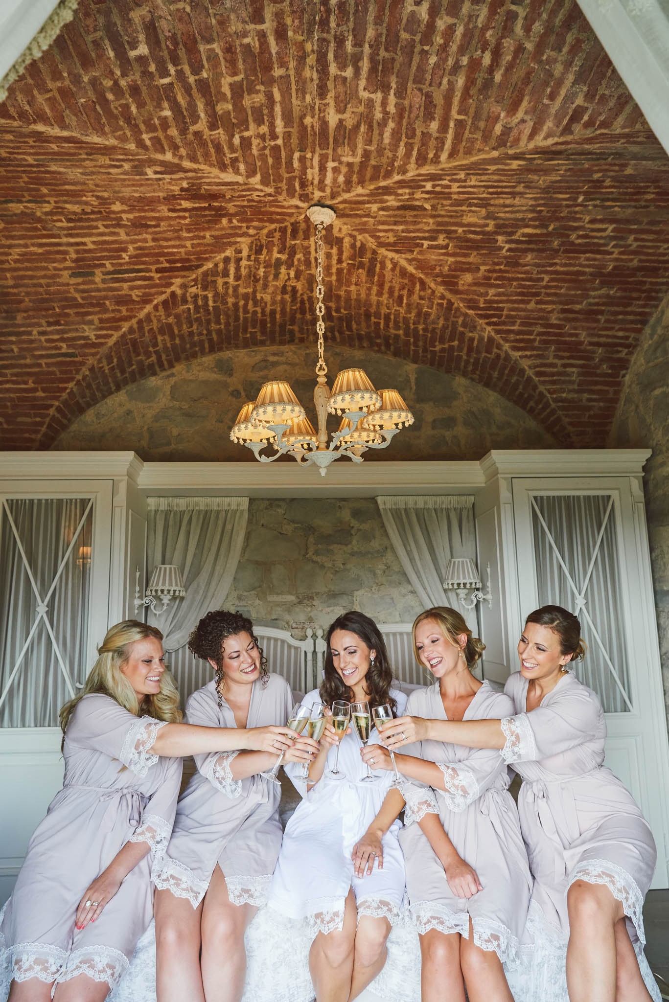 bridesmaids in dressing gowns toasting champagne in a rustic brick room