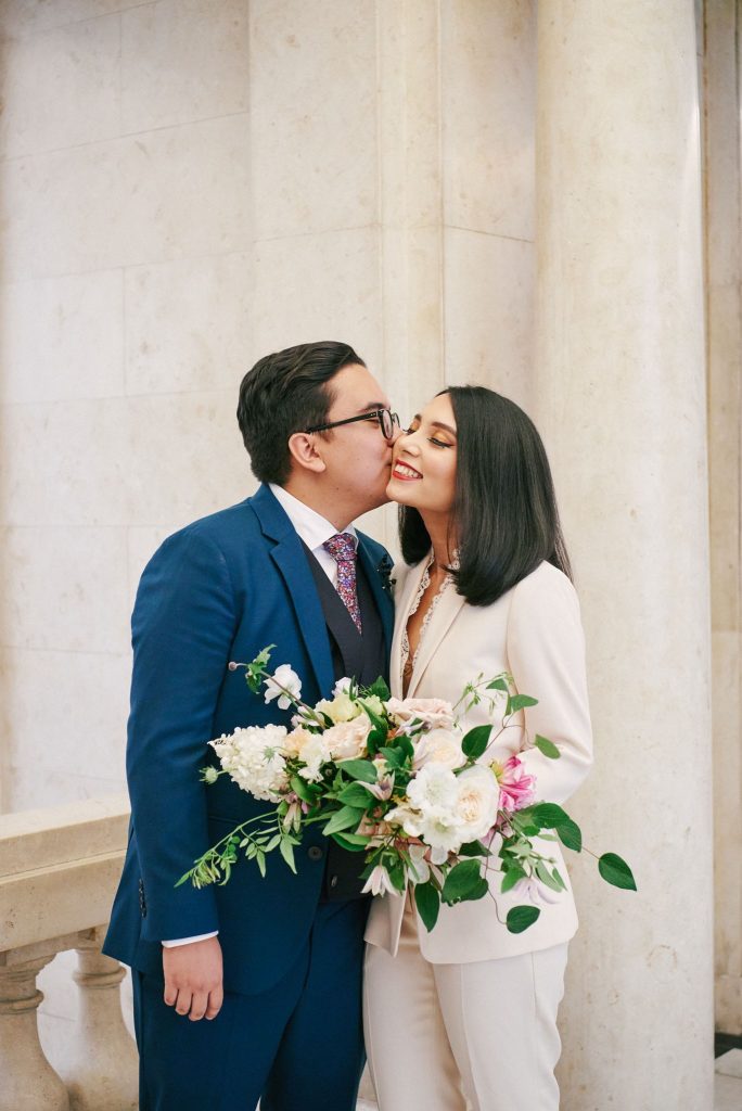 Bride and groom kissing in front of white marble at Old Marylebone Town Hall in Central London.