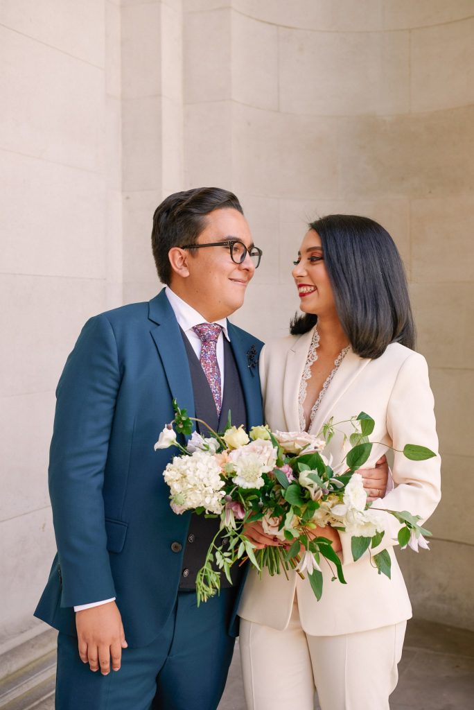 Bride and groom smiling together in front of the stone walls outside The Old Marylebone Town Hall