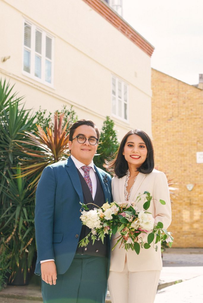 Bride and groom smiling together on a brick street with green plants in Marylebone, London.