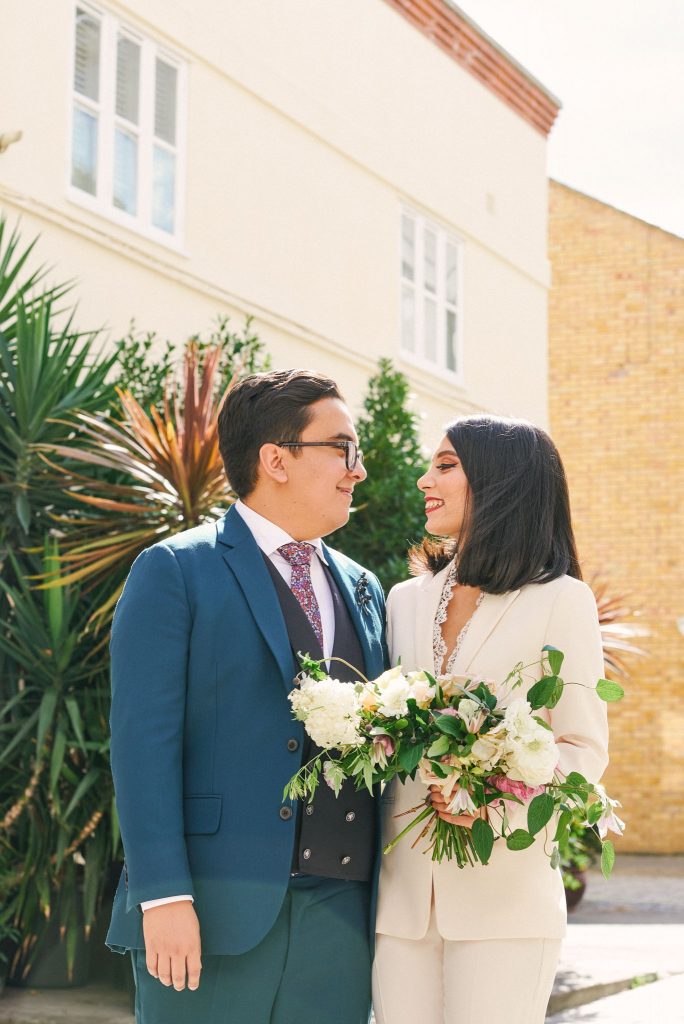 Bride and groom smiling together on a sunny day on a brick street in Marylebone, London.