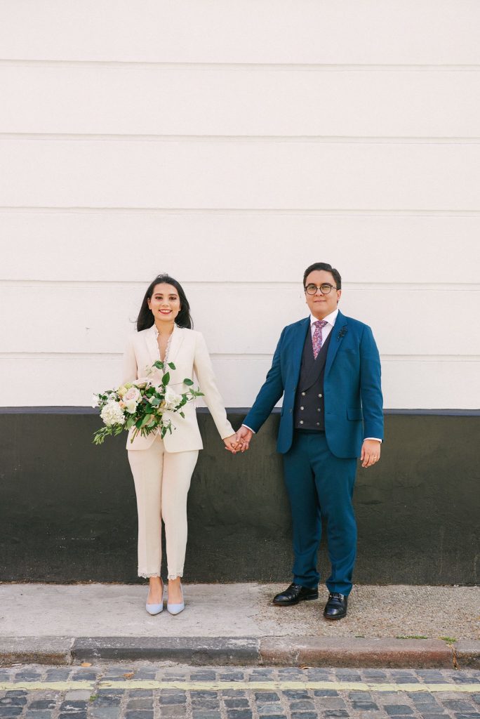 Bride and groom holding hands in front of black and white wall in central London. 