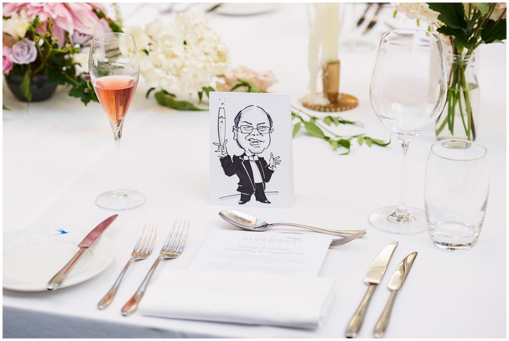 Caricature drawing of a wedding guest next to champagne on a table at The Bluebird in Chelsea