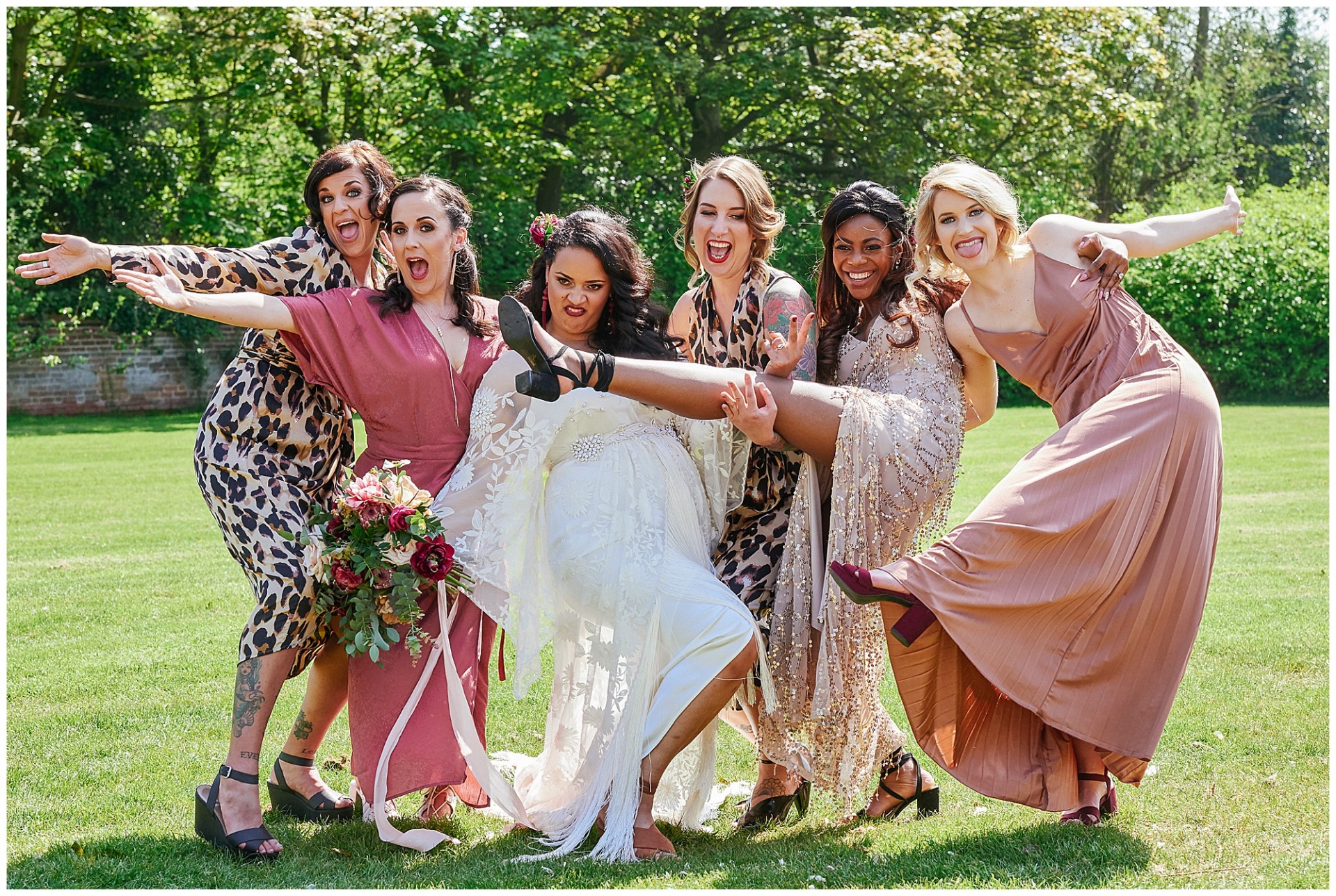 Bride with bridesmaids doing silly poses the field at Walled Garden in Beeston