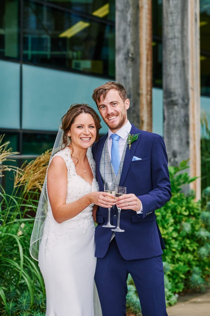 Bride and groom smiling and holding champagne outside of the Oyster Shed 