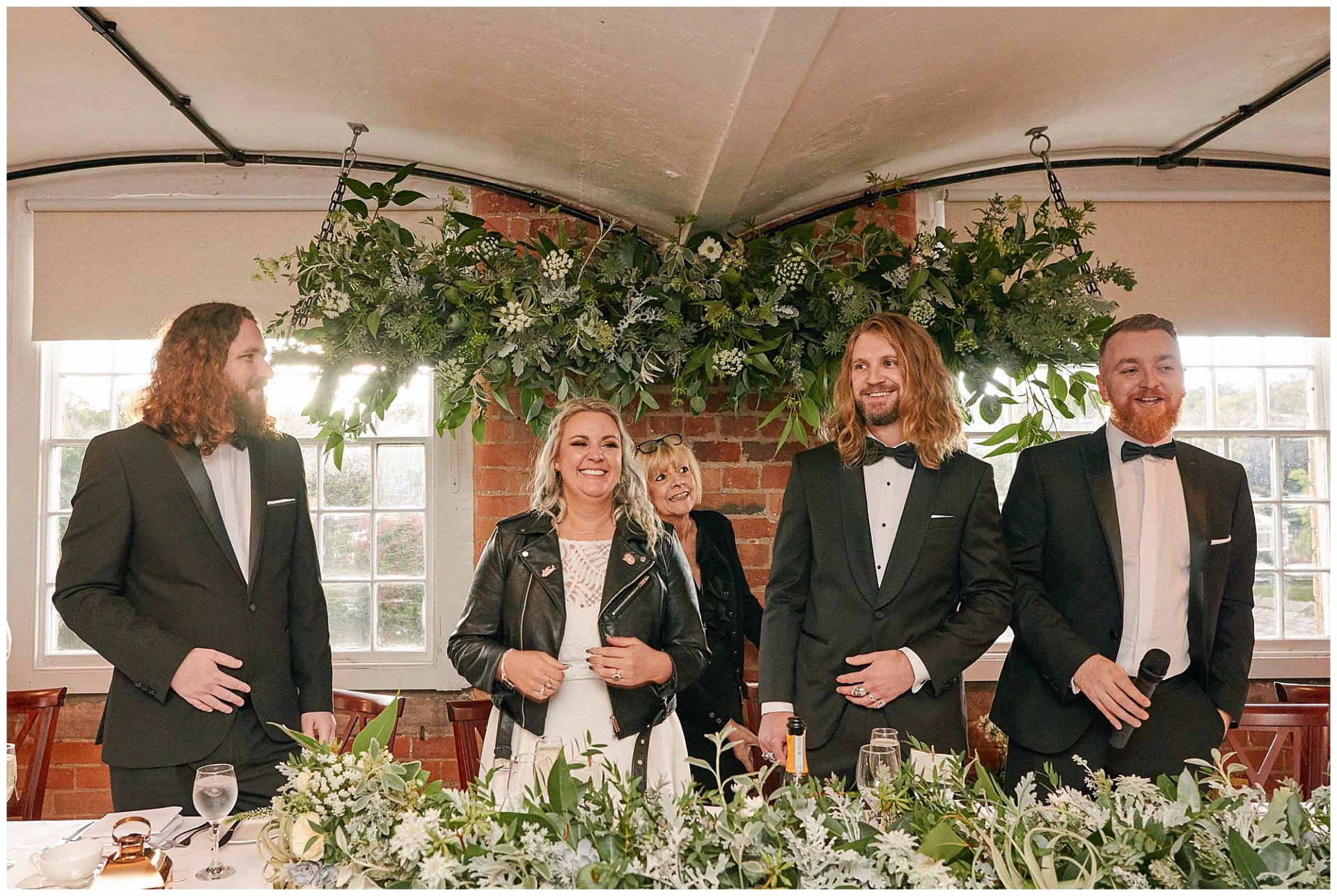 Bride and groom with best men laughing at the top table in front of a brick wall at the West Mill in Derby.