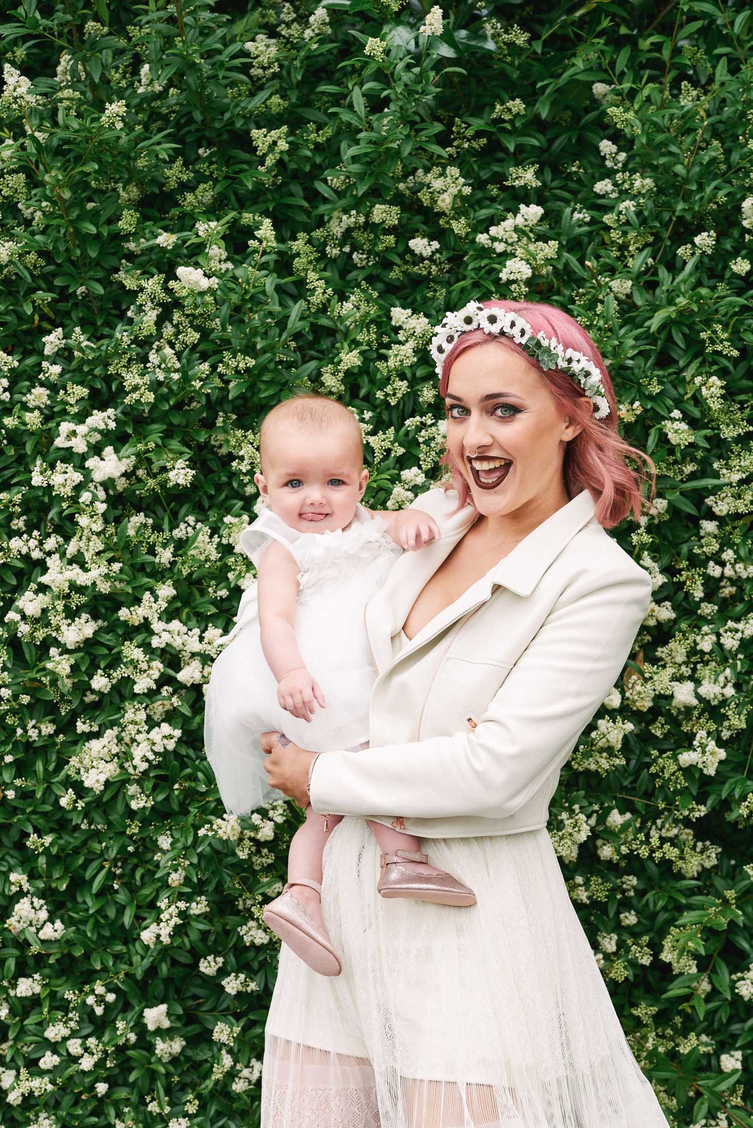 Bride with pink hair wearing a white leather jacket and holding a baby
