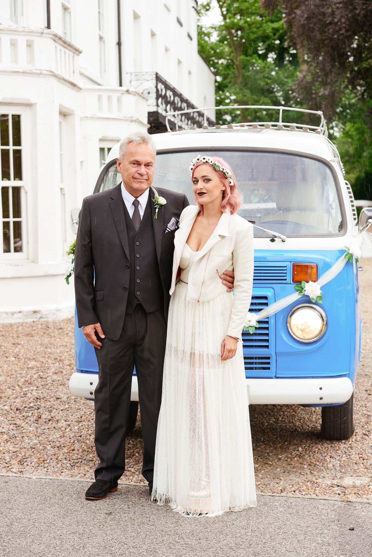 Bride with pink hair stood with her dad in front of festival style VW Camper van