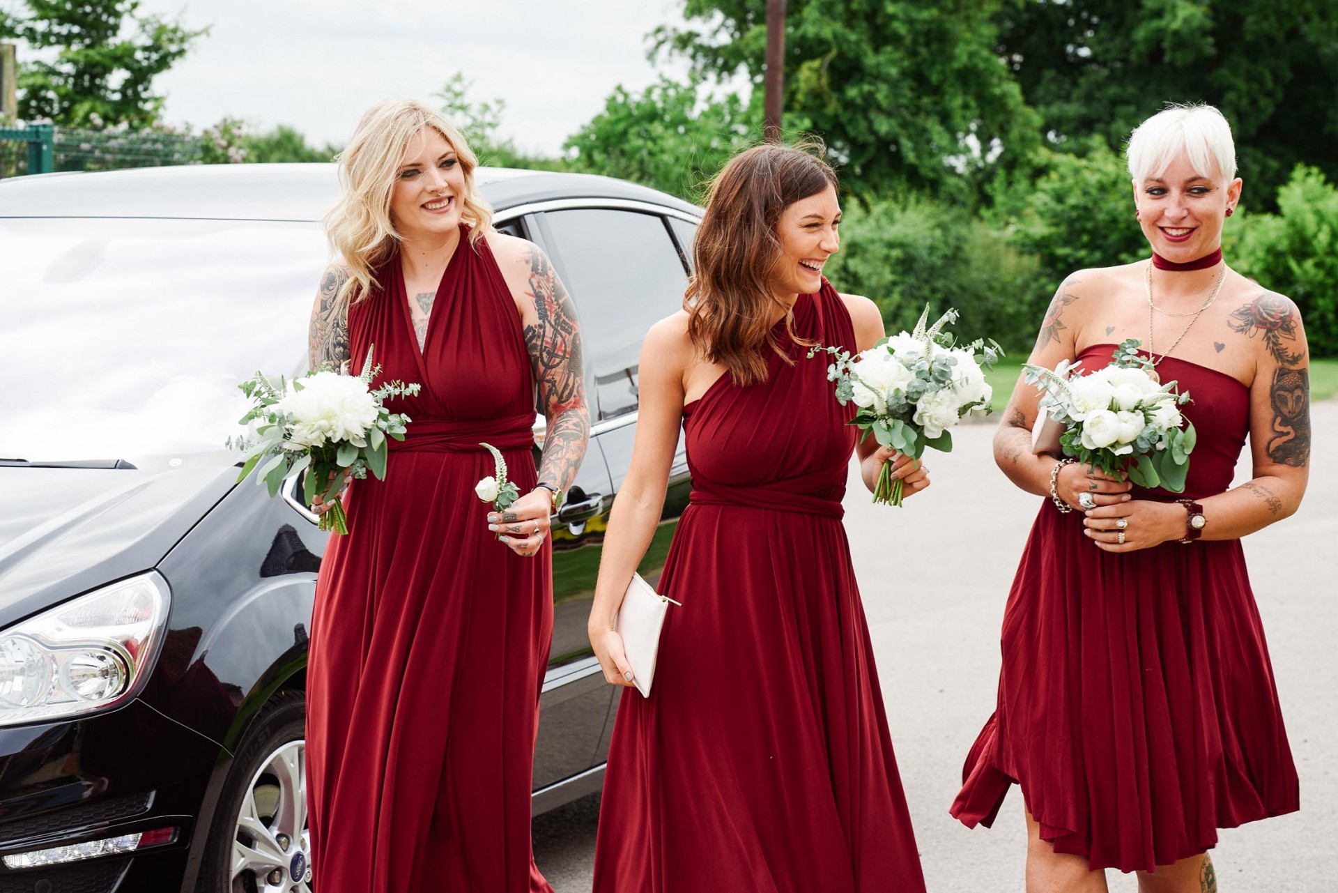 Tattooed bridesmaids wearing red dresses arriving at Pheasantry Brewery wedding venue