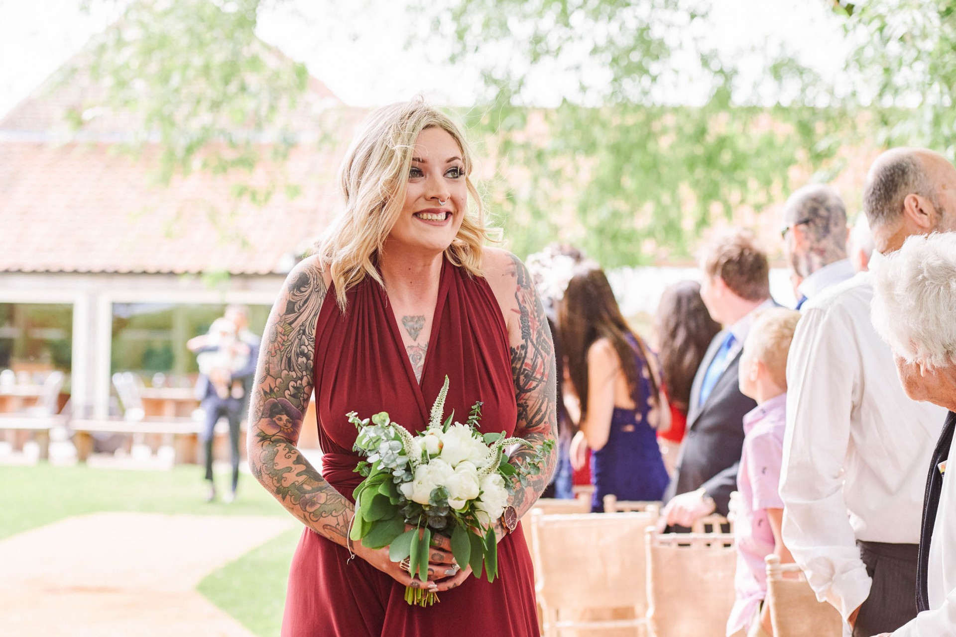 Tattooed bridesmaid walking down outdoor wedding aisle at The Pheasantry Brewery