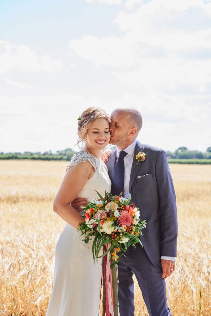 Bride and groom laughing together whilst stood in a field on a sunny day at The Granary Estates in Cambridge