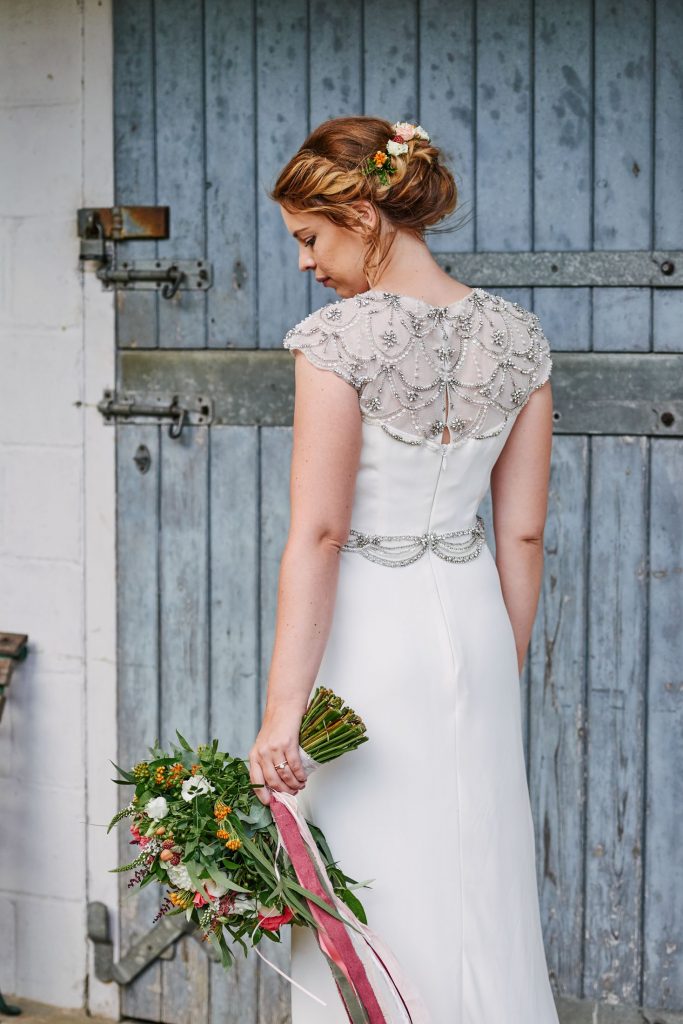 back of brides white wedding dress with flowers in her hand against a blue barn door in Cambridge