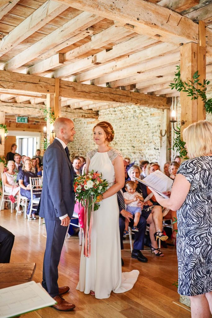 Bride and groom smiling at each other during wedding ceremony at The Granary Estates stone barn in Cambridge.