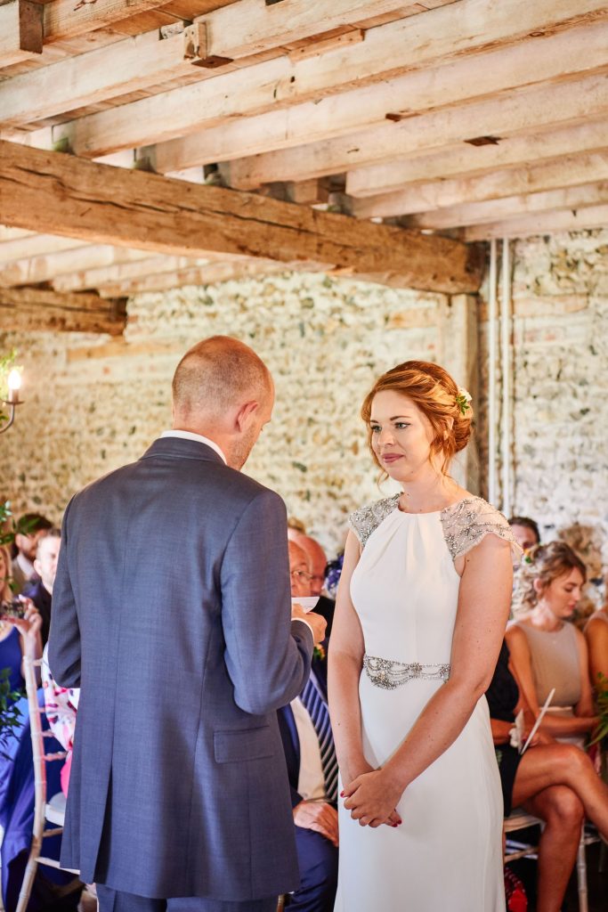 Bride and groom smiling at each other during wedding ceremony at The Granary Estates stone barn in Cambridge.