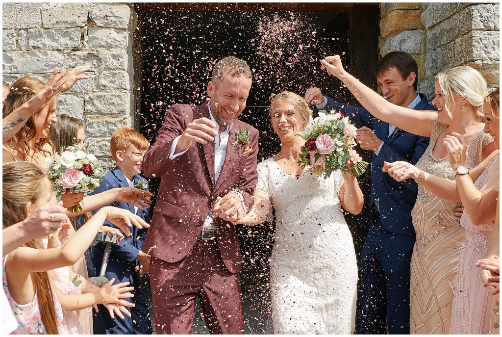 Bride and groom exiting the stone barn while guests throw confetti at them