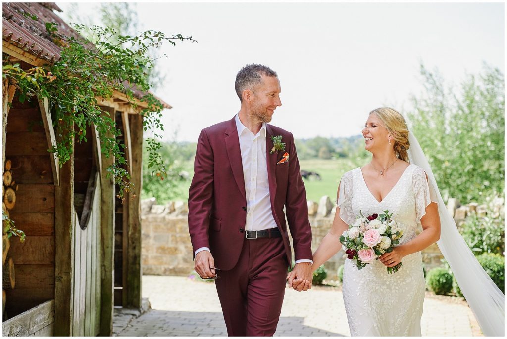 bride and groom walking together holding hands next to a barn in the countryside