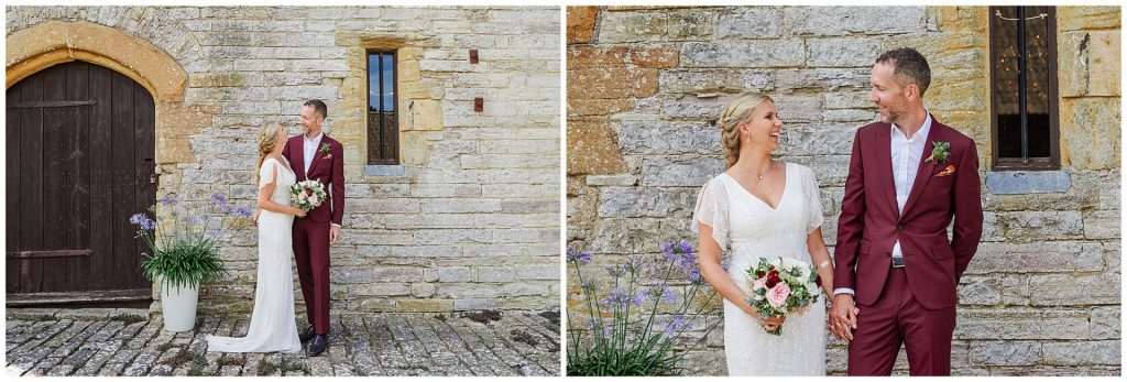 Bride and groom smiling together in front of old stone barn building on their wedding day