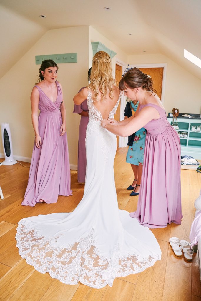 Bridesmaids helping to button up brides beautiful white lace dress