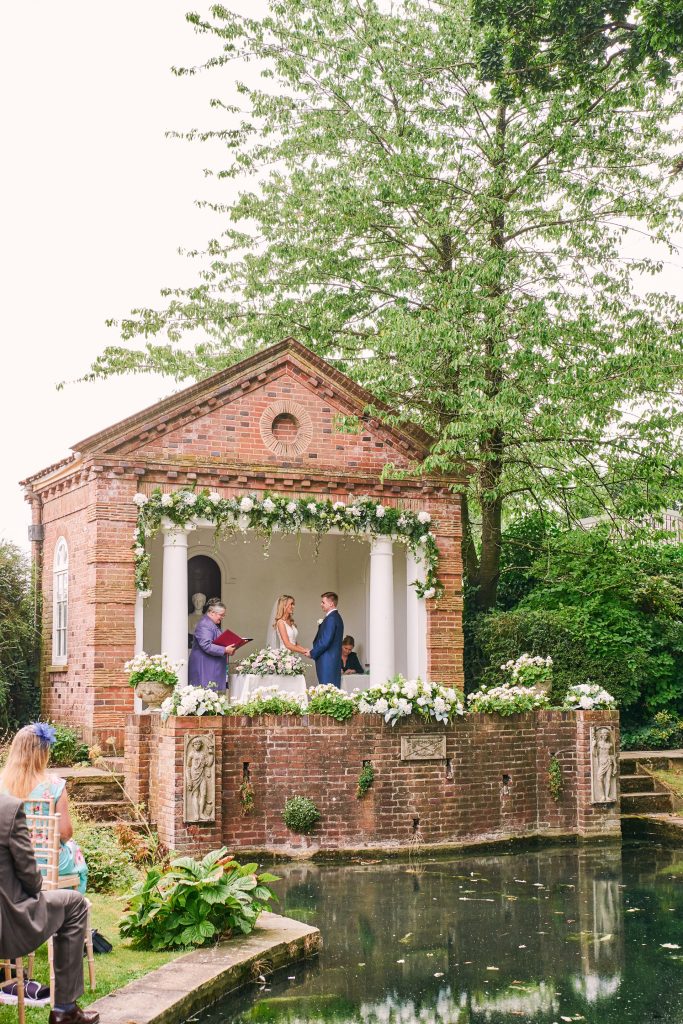 Bride and groom during outdoor garden wedding ceremony in front of a pond