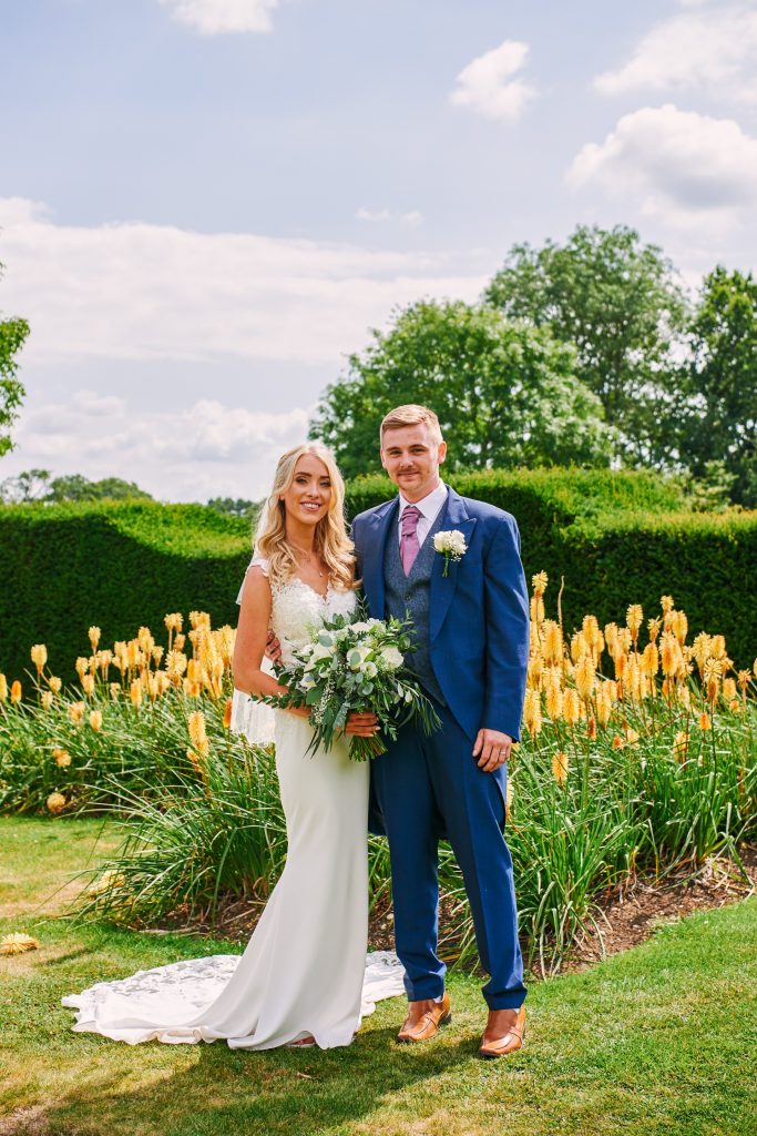 Bride and groom in front of yellow flowers in the gardens at Micklefield Hall