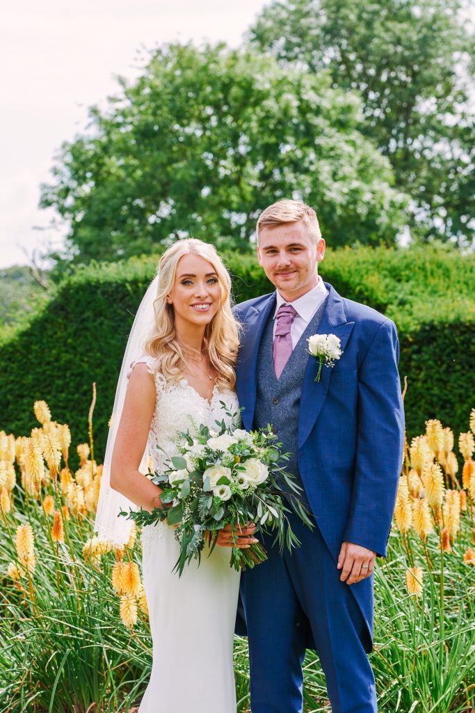 Bride and groom stood in front of yellow flowers on a beautiful sunny day
