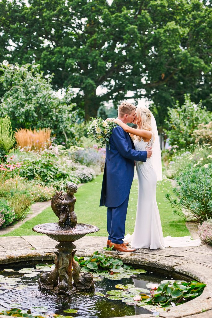 Wedding couple kissing in front of a fountain in beautiful country garden