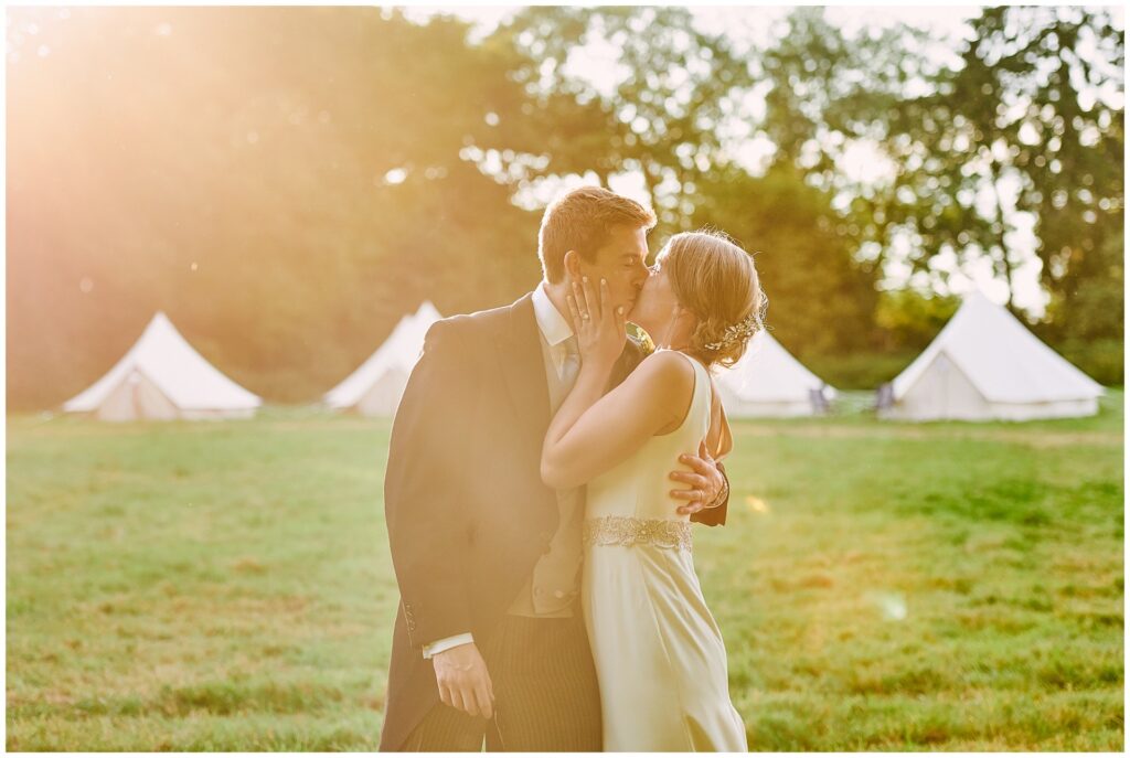 bride and groom kissing in front of festival tents during sunset