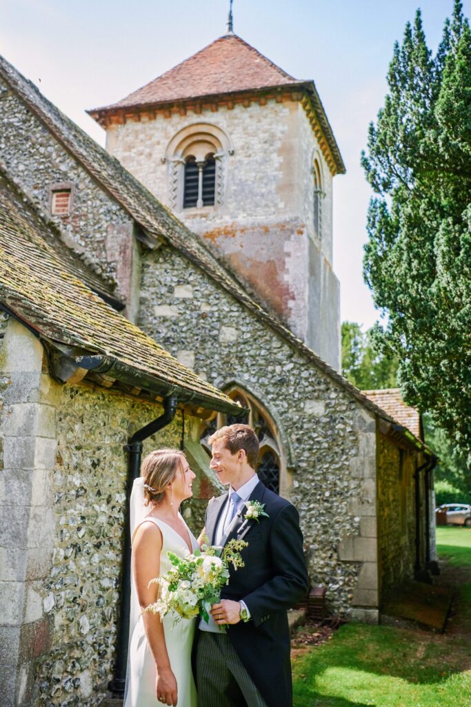 wedding couple smiling at each other outside of a church on a sunny day