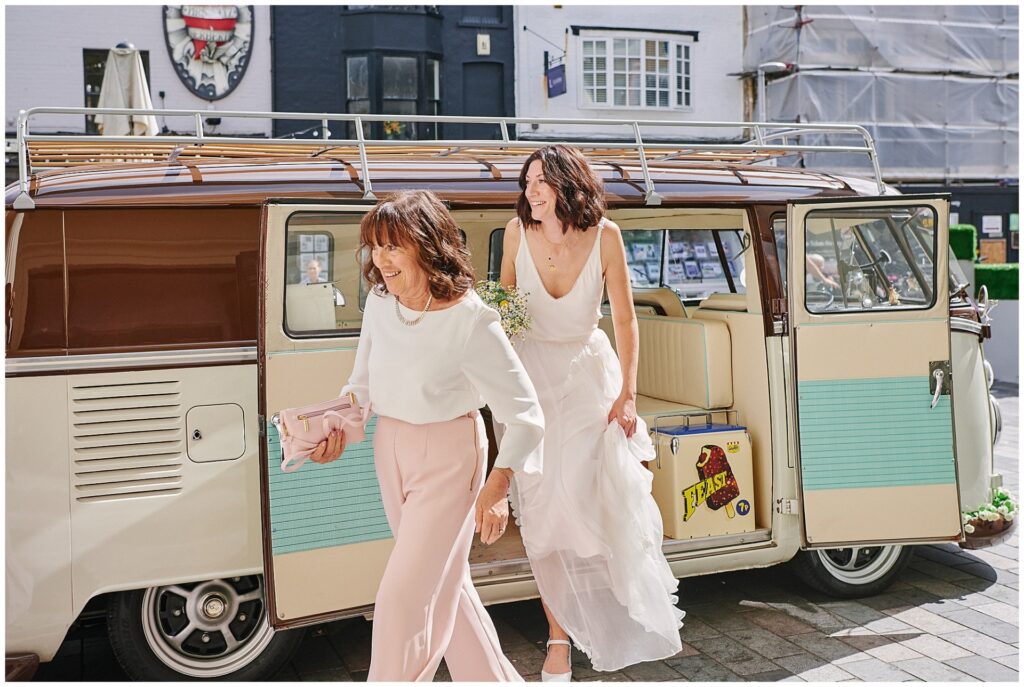 Happy bride stepping out of VW camper van on her wedding day in Brighton 