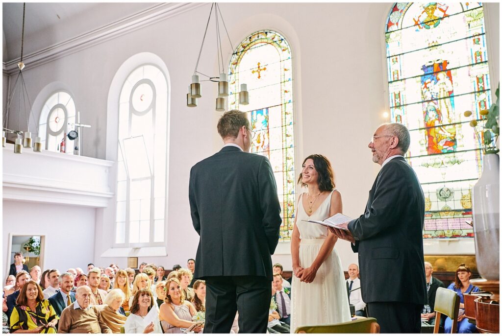 Bride and groom smiling during wedding ceremony in front of friends and family.
