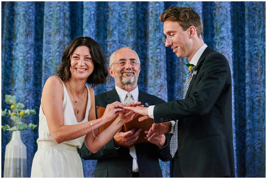 Bride laughing as she exchanges wedding rings with groom at Brighton Unitarian Church