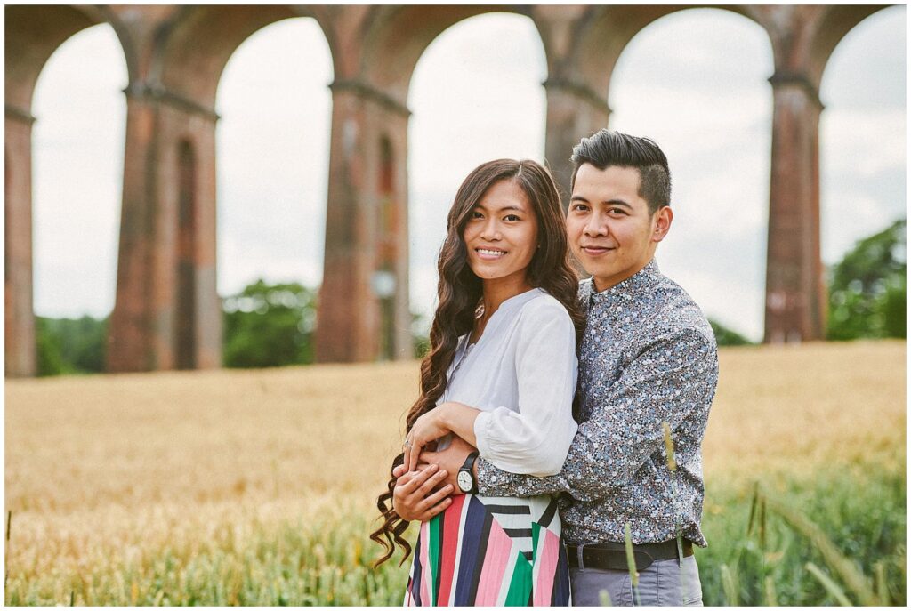 Engaged couple smiling whilst holding each other in front of The Ouse Valley Viaduct