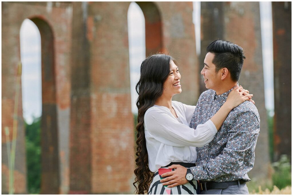 Engaged couple hugging in font of brick arches in Sussex during engagement shoot