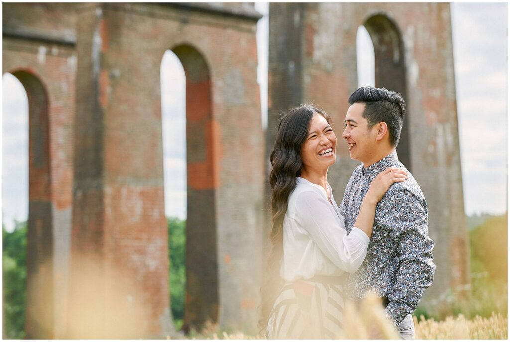 Happy couple laughing together whilst stood under The Ouse Valley Viaduct surrounded by brick