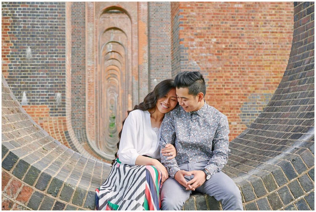Happy wedding couple sat on a brick wall laughing together