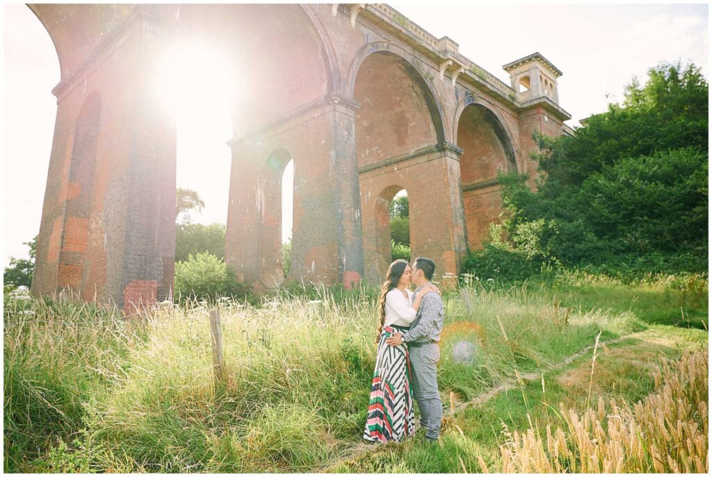 Engaged couple kissing at sunset in front of The Ouse Valley Viaduct