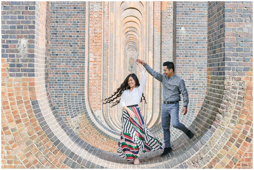 Engaged couple dancing on top of a brick wall under The Ouse Valley Viaduct