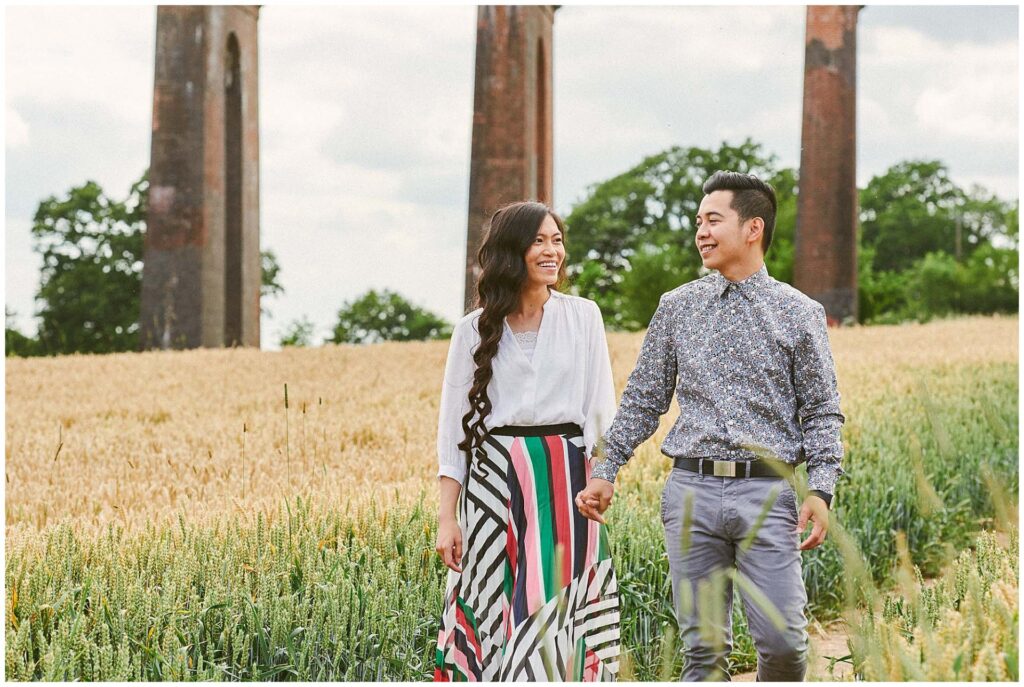 Happy couple walking through a field in front of The Ouse Valley Viaduct