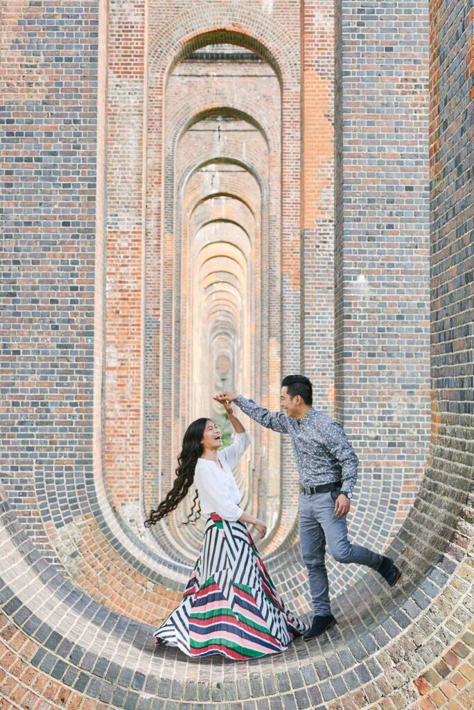 Engaged couple dancing on top of a brick wall under The Ouse Valley Viaduct