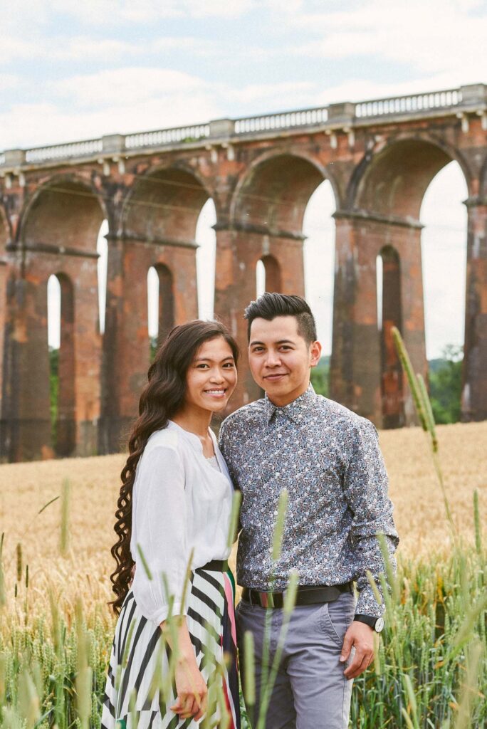 Engaged couple smiling in a field in front of The Ouse Valley Viaduct