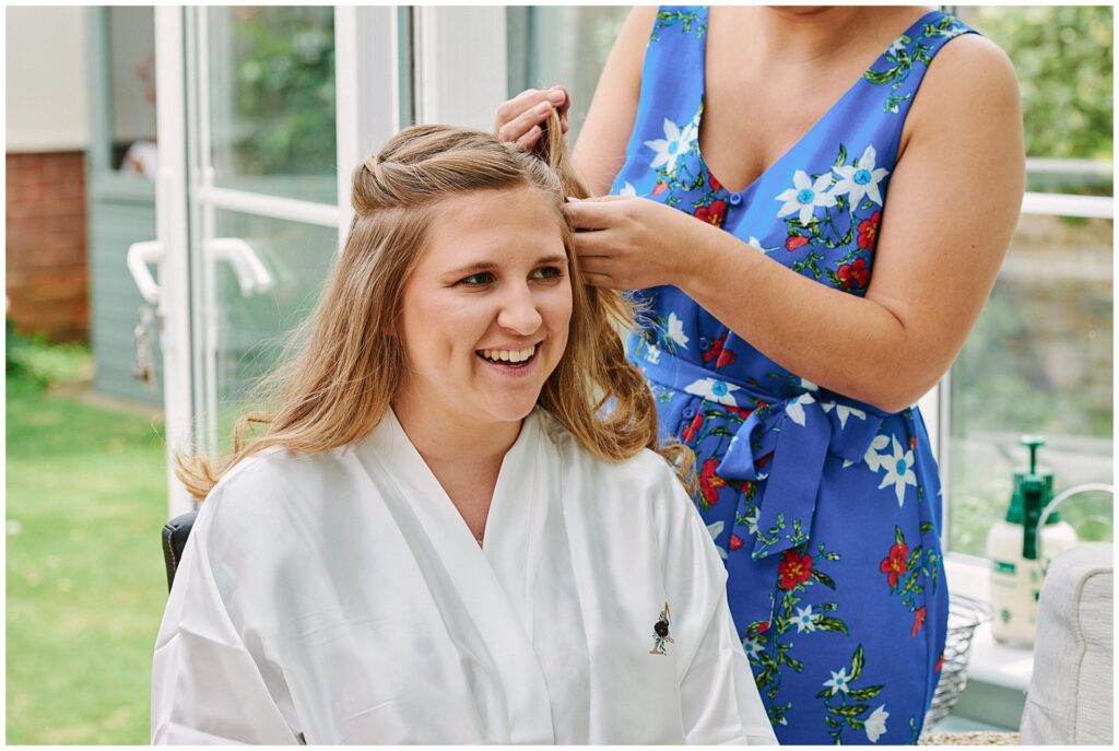 Relaxed bride in dressing gown having her hair styled in Essex