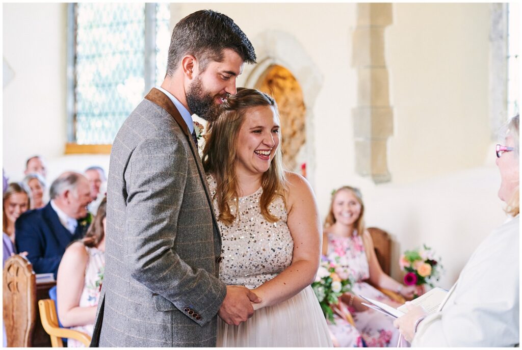 Bride and groom smiling and holding hands during wedding ceremony in Essex